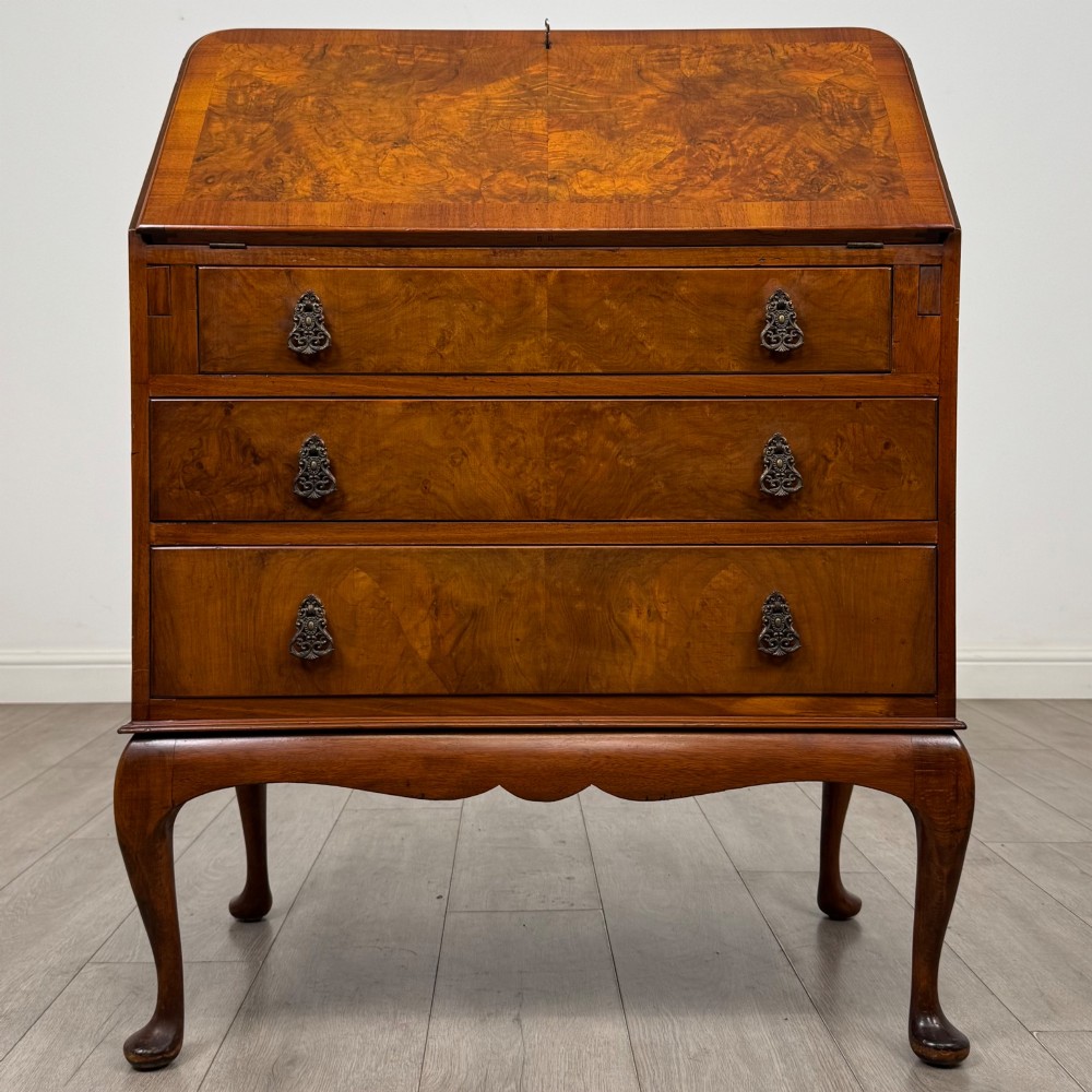 An Edwardian figured walnut writing bureau featuring a slant front above three drawers and carved cabriole legs.