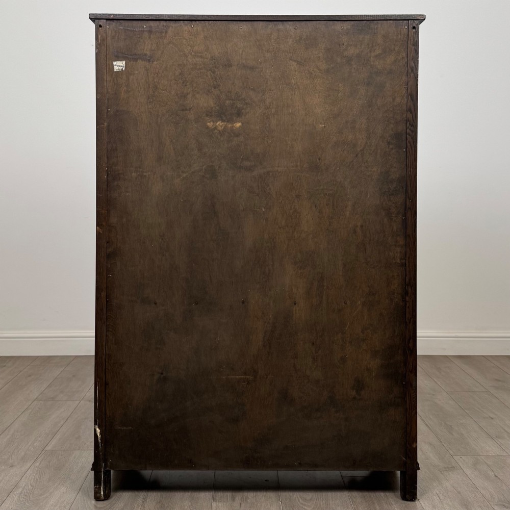A dark oak display cabinet featuring two upper leaded glass doors, lower cupboard doors carved with linenfold panels, and decorative metal hinges. View VI