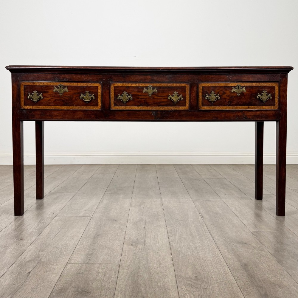 An antique dark oak dresser base featuring three crossbanded drawers with brass drop handles and keyhole escutcheons, supported by four straight square legs.