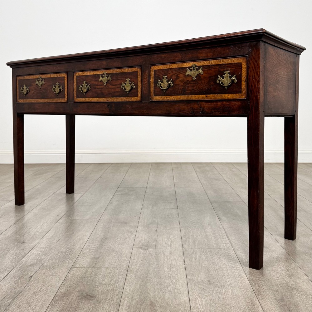 An antique dark oak dresser base featuring three crossbanded drawers with brass drop handles and keyhole escutcheons, supported by four straight square legs. View II