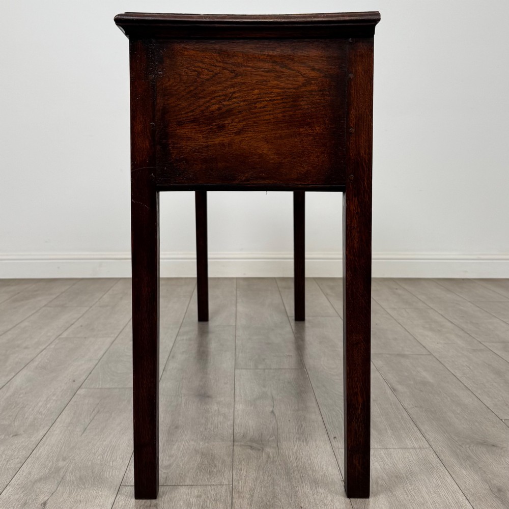 An antique dark oak dresser base featuring three crossbanded drawers with brass drop handles and keyhole escutcheons, supported by four straight square legs. View III