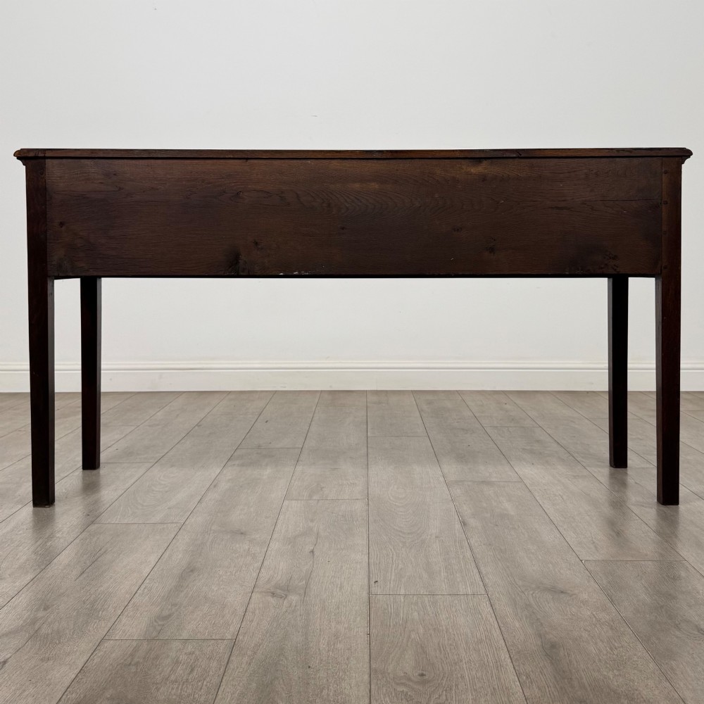 An antique dark oak dresser base featuring three crossbanded drawers with brass drop handles and keyhole escutcheons, supported by four straight square legs. View V