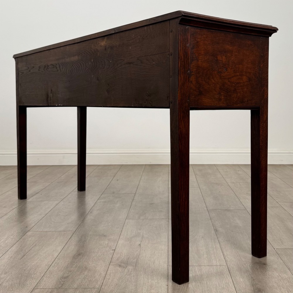 An antique dark oak dresser base featuring three crossbanded drawers with brass drop handles and keyhole escutcheons, supported by four straight square legs. View VI