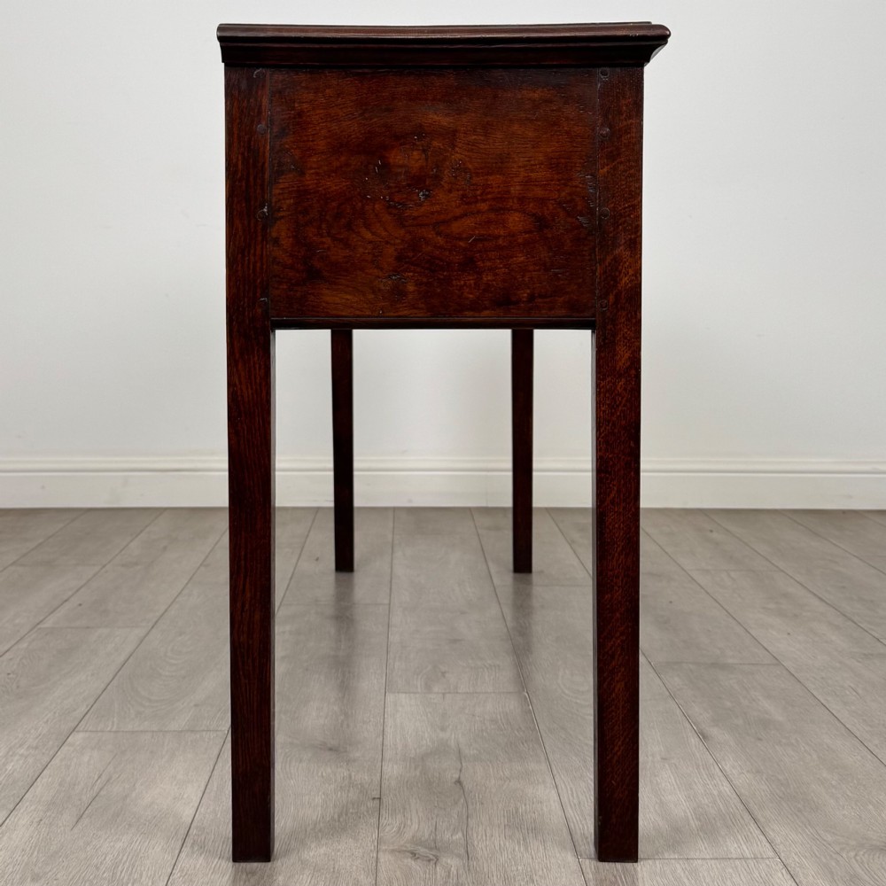 An antique dark oak dresser base featuring three crossbanded drawers with brass drop handles and keyhole escutcheons, supported by four straight square legs. View VII