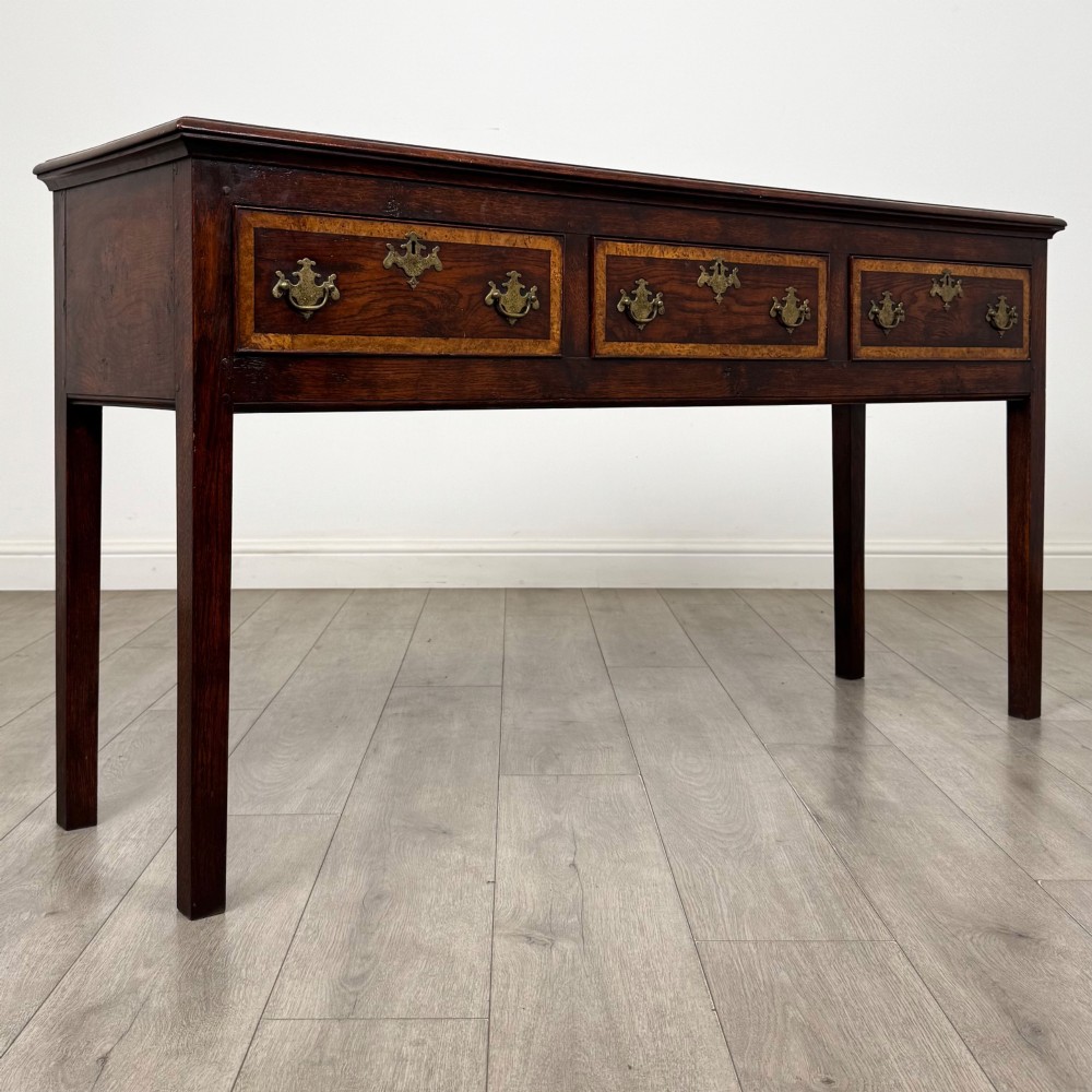 An antique dark oak dresser base featuring three crossbanded drawers with brass drop handles and keyhole escutcheons, supported by four straight square legs. View VIII