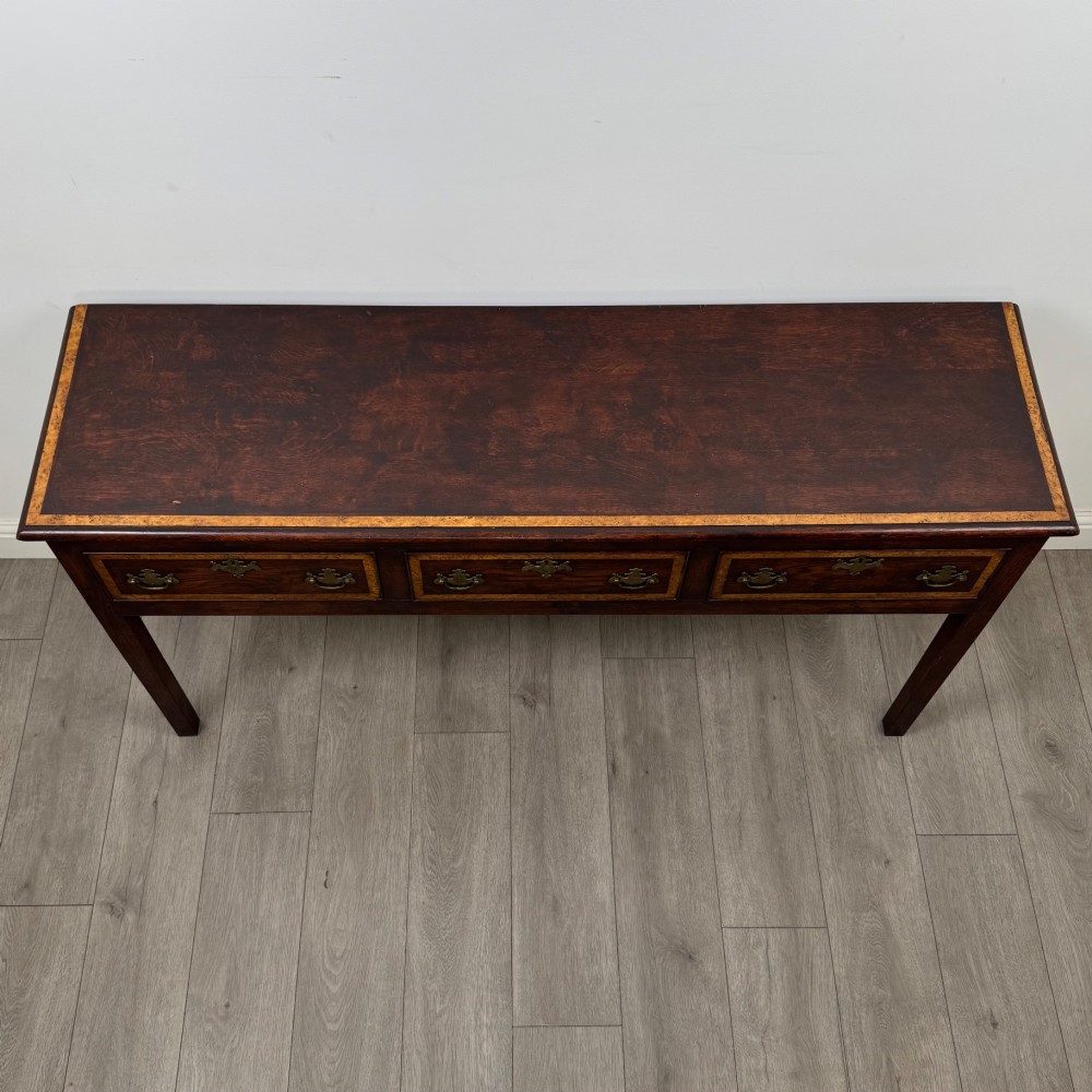 An antique dark oak dresser base featuring three crossbanded drawers with brass drop handles and keyhole escutcheons, supported by four straight square legs. View IX