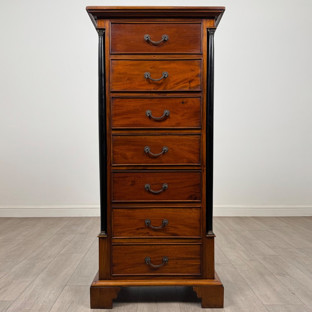 A tall, narrow mahogany chest featuring seven drawers flanked by dark ebonised side columns on bracket feet.
