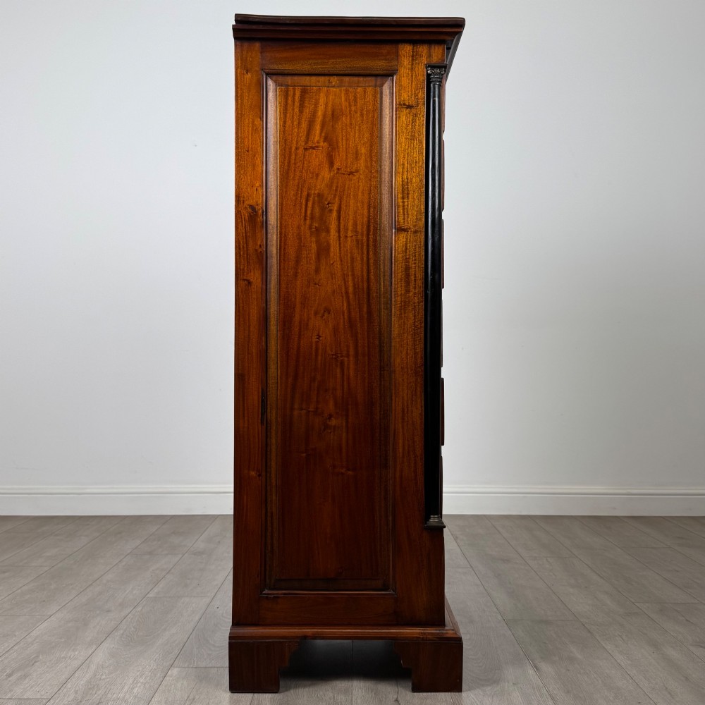 A tall, narrow mahogany chest featuring seven drawers flanked by dark ebonised side columns on bracket feet. View VII