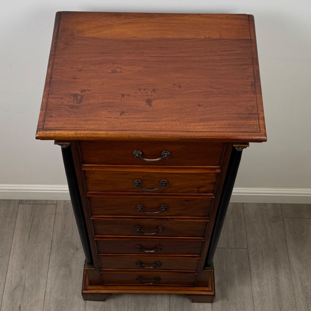 A tall, narrow mahogany chest featuring seven drawers flanked by dark ebonised side columns on bracket feet. View IX
