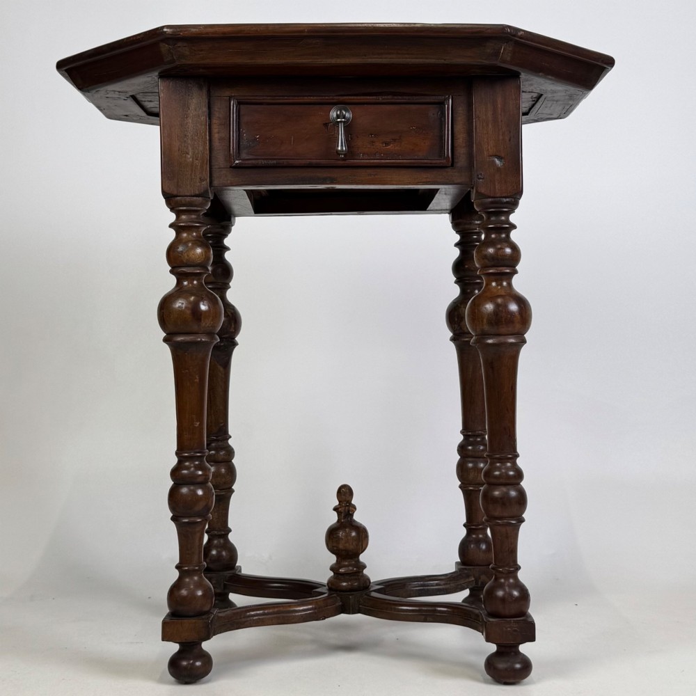 A dark brown hardwood octagonal side table with turned legs, a single drawer with a brass pull, and an arched cross-stretcher featuring a central finial.