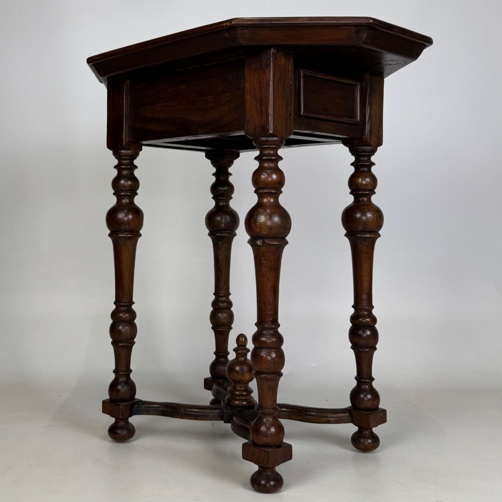 A dark brown hardwood octagonal side table with turned legs, a single drawer with a brass pull, and an arched cross-stretcher featuring a central finial. View VI
