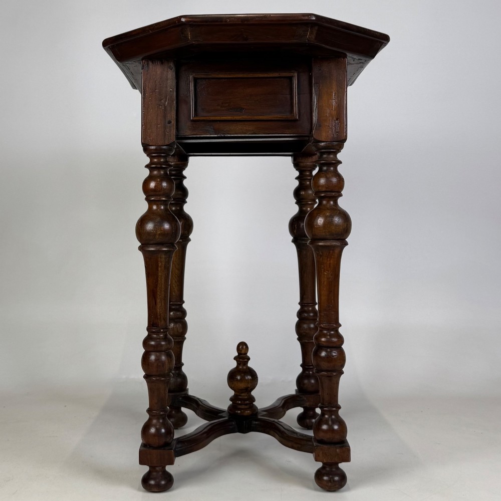 A dark brown hardwood octagonal side table with turned legs, a single drawer with a brass pull, and an arched cross-stretcher featuring a central finial. View VII