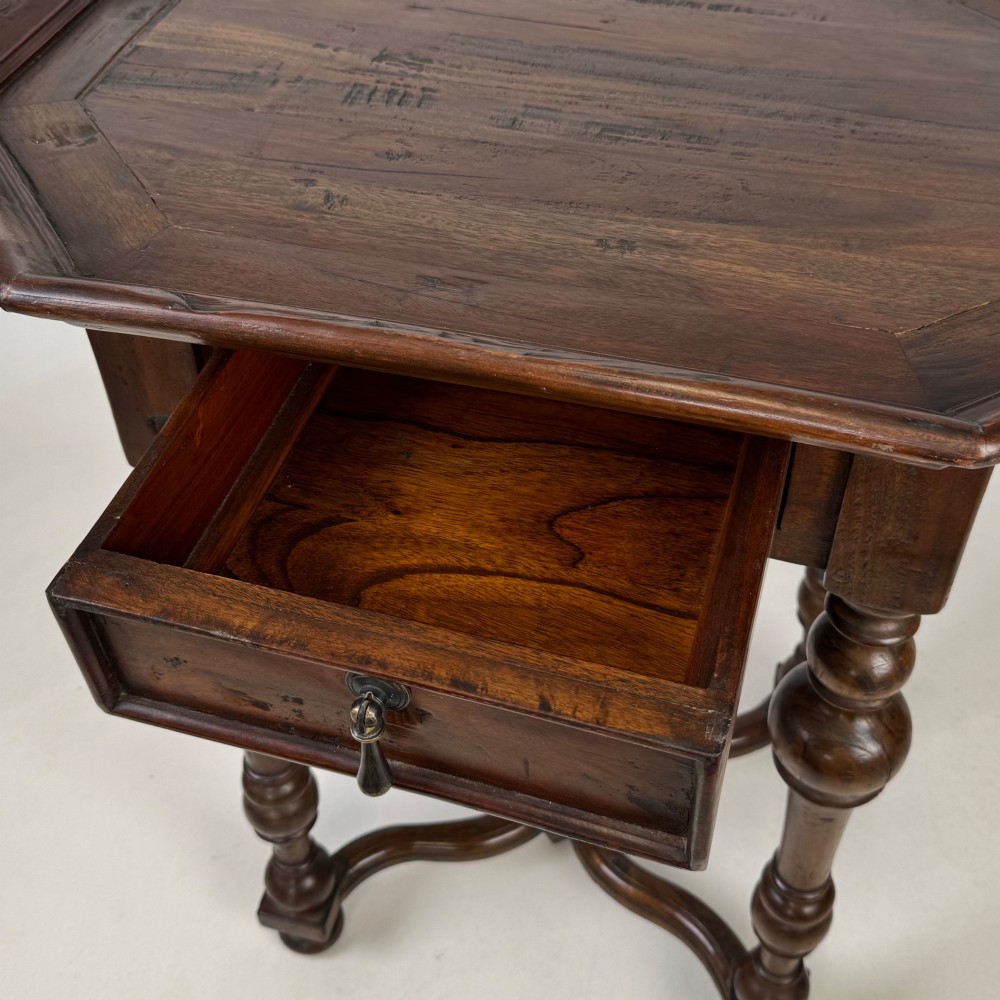 A dark brown hardwood octagonal side table with turned legs, a single drawer with a brass pull, and an arched cross-stretcher featuring a central finial. View X