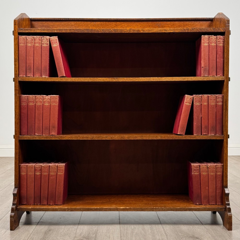 An early twentieth-century open golden oak bookcase featuring four wide wooden shelves and shaped side profile base.