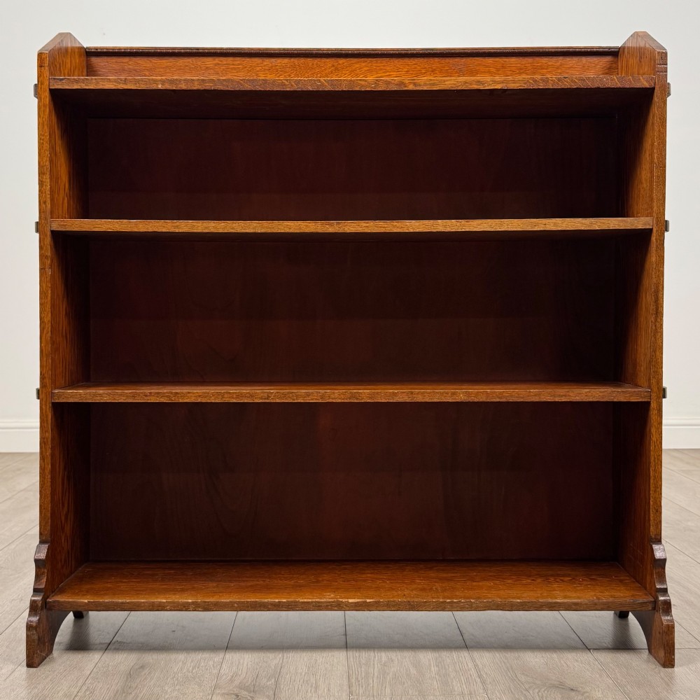 An early twentieth-century open golden oak bookcase featuring four wide wooden shelves and shaped side profile base. View II