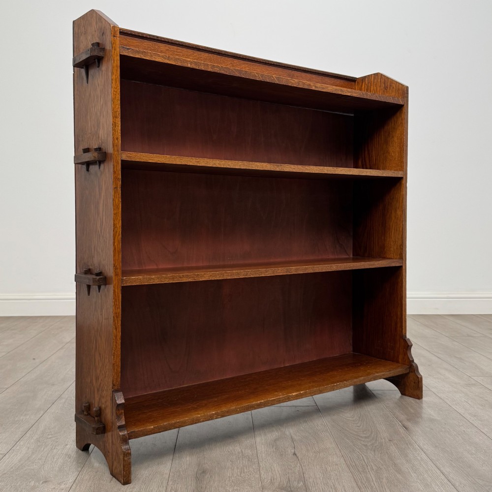 An early twentieth-century open golden oak bookcase featuring four wide wooden shelves and shaped side profile base. View IX