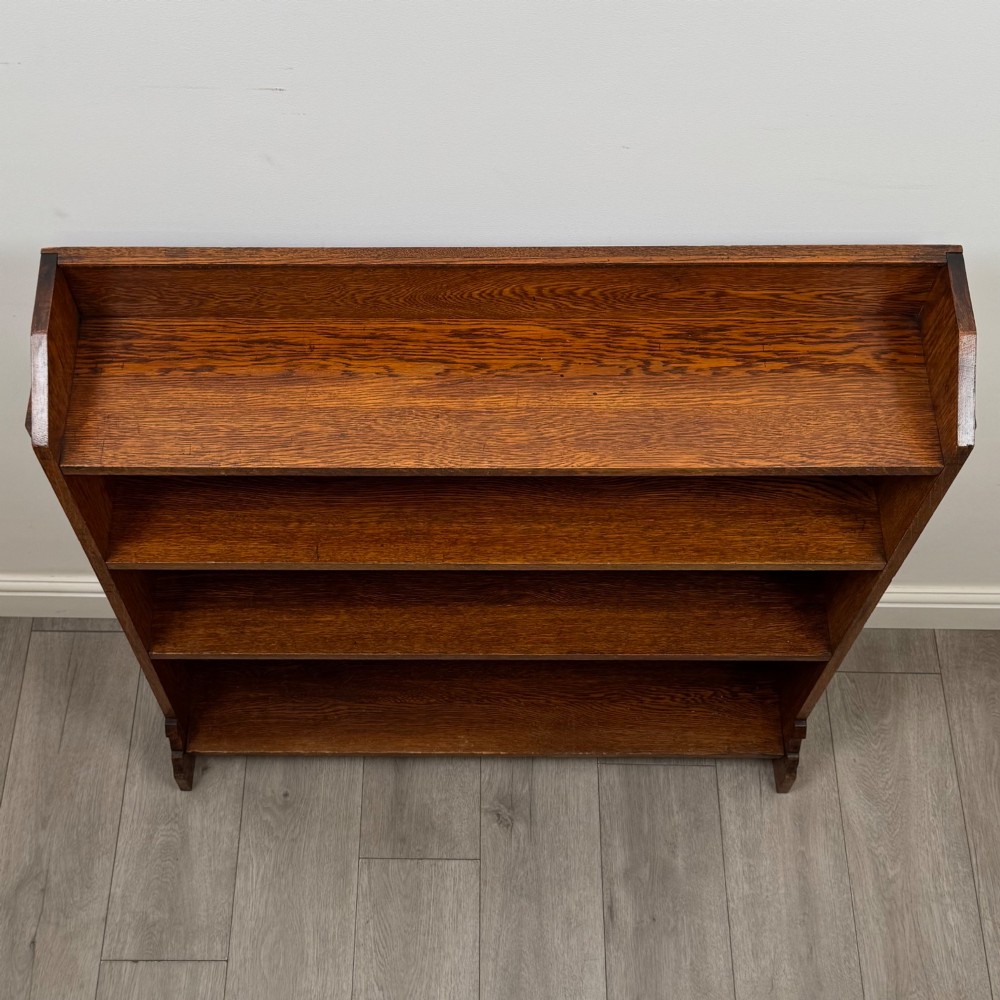An early twentieth-century open golden oak bookcase featuring four wide wooden shelves and shaped side profile base. View X