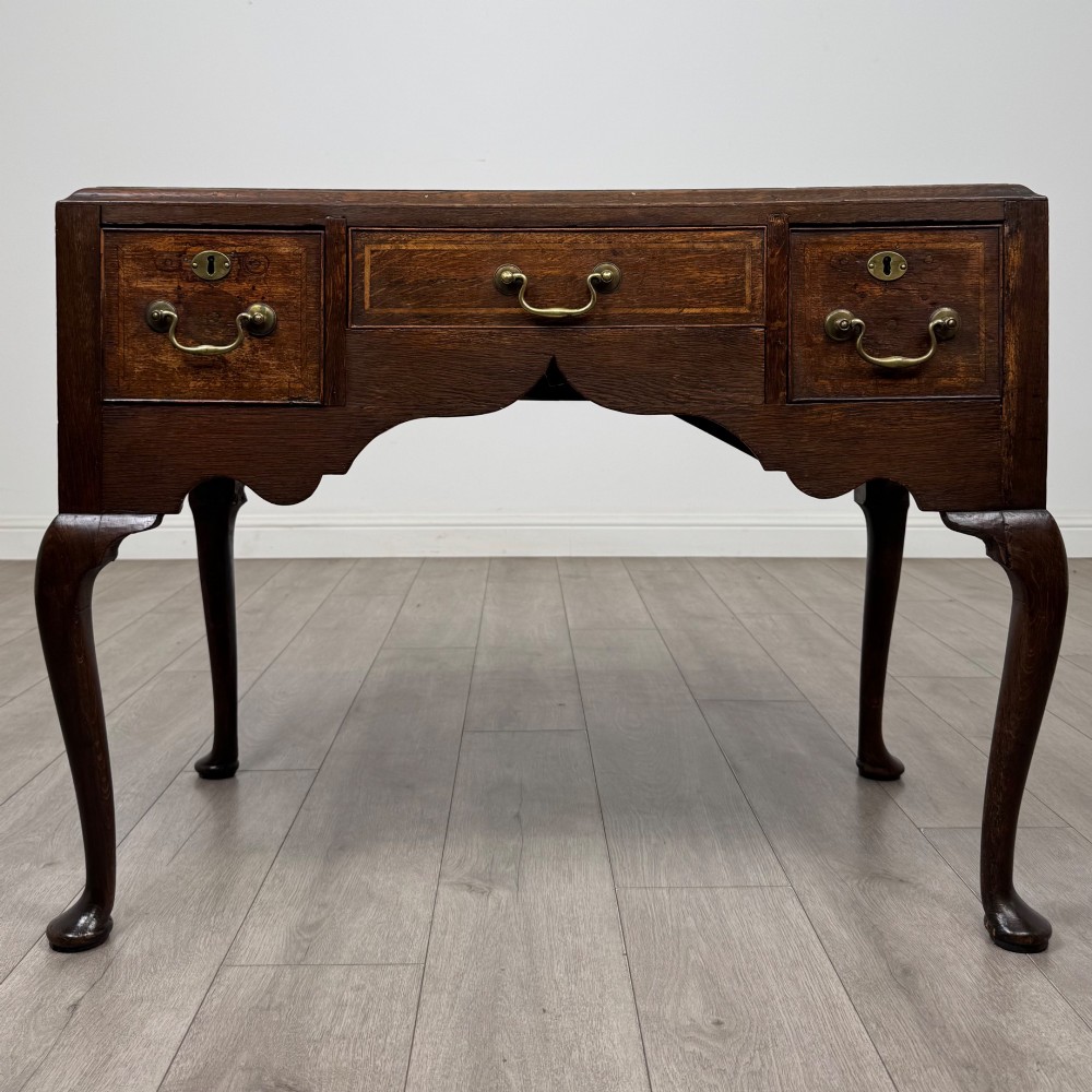 An 18th-century Georgian oak side table featuring three drawers with brass drop handles, an arched apron, and cabriole legs.