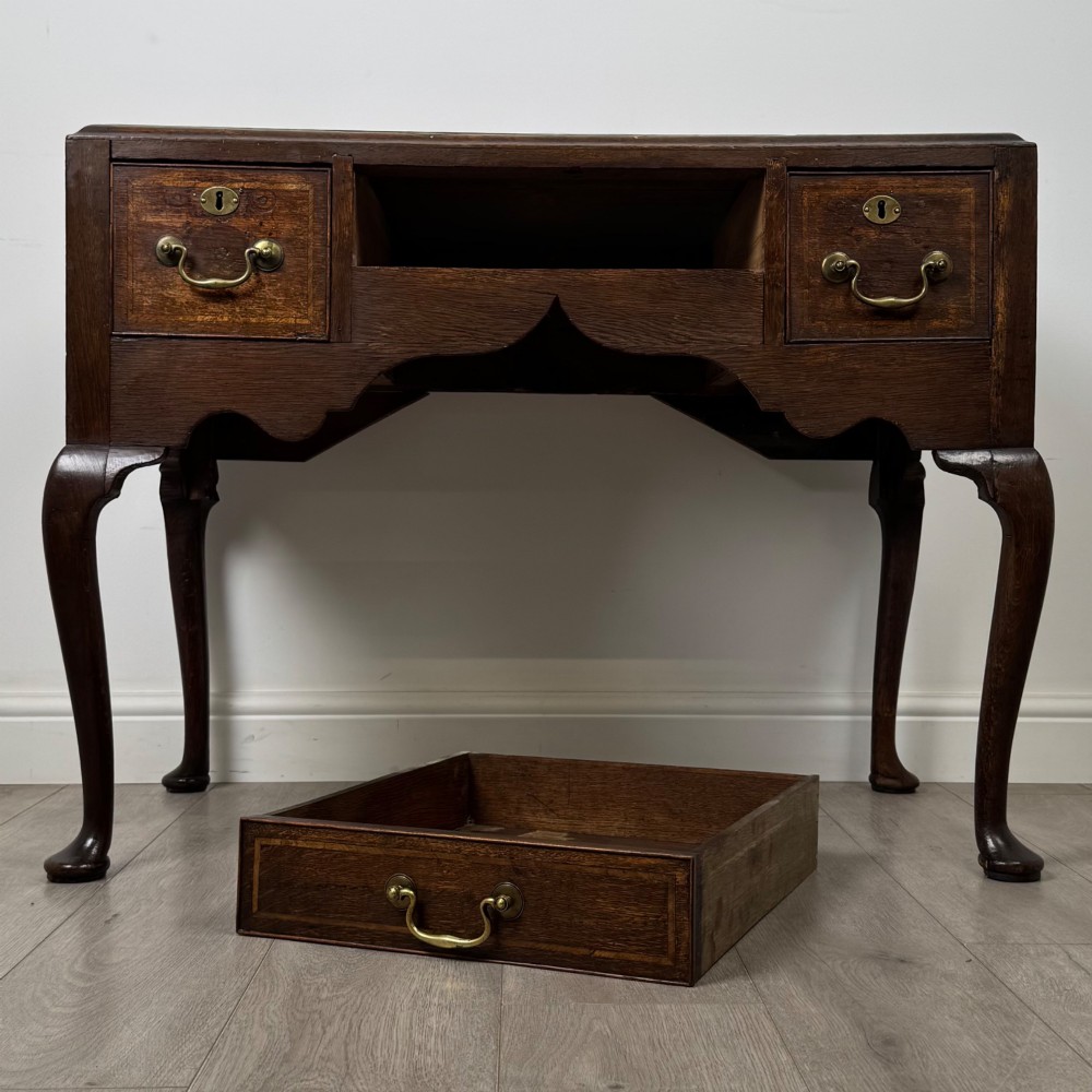 An 18th-century Georgian oak side table featuring three drawers with brass drop handles, an arched apron, and cabriole legs. View X