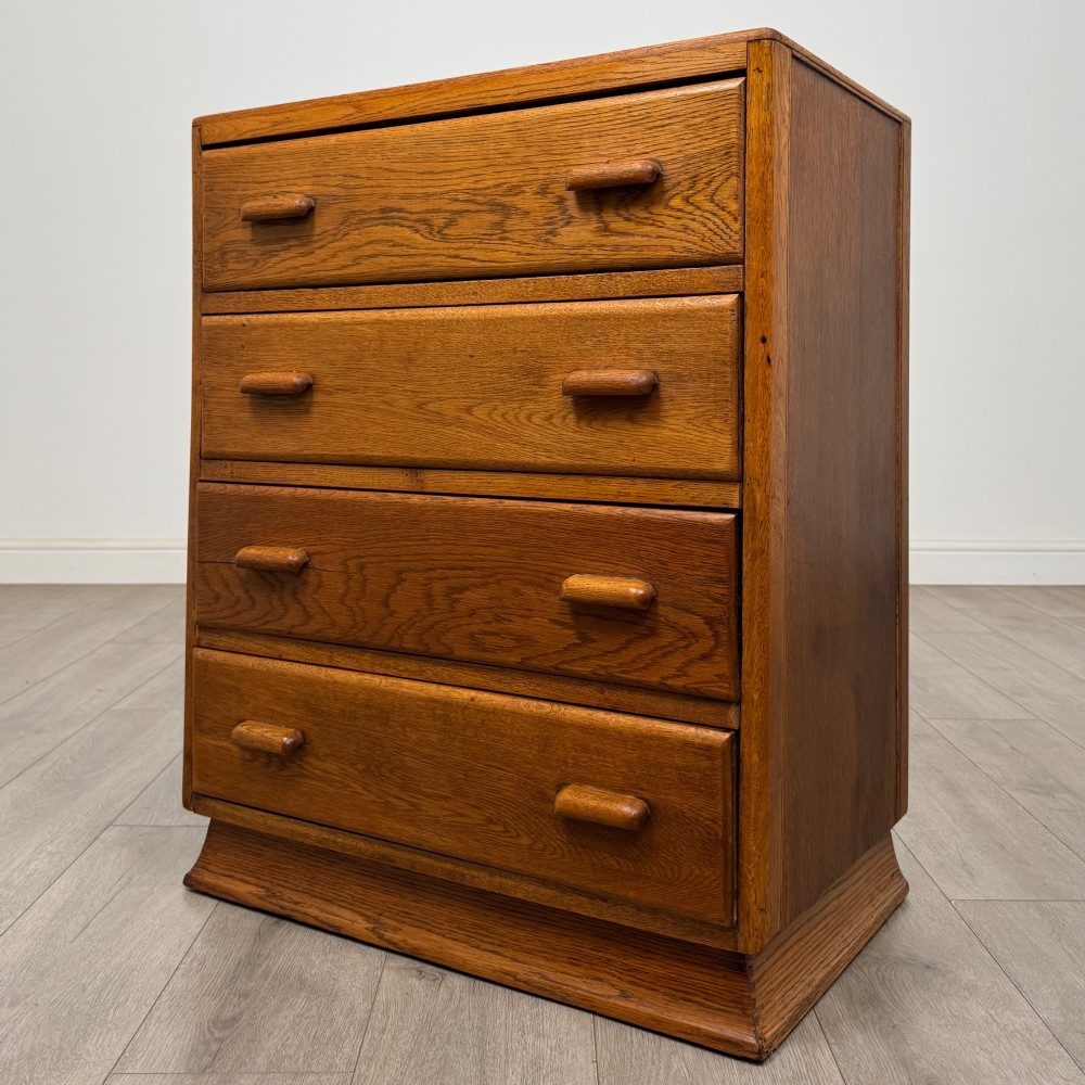 A vintage medium-toned oak chest of drawers featuring four graduated drawers with matching wooden bar handles set on a flared plinth base. View II