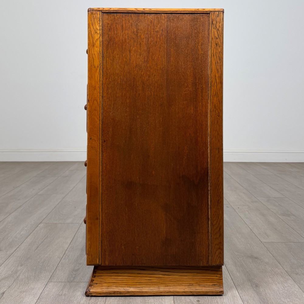 A vintage medium-toned oak chest of drawers featuring four graduated drawers with matching wooden bar handles set on a flared plinth base. View III