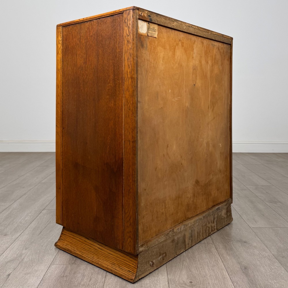 A vintage medium-toned oak chest of drawers featuring four graduated drawers with matching wooden bar handles set on a flared plinth base. View IV