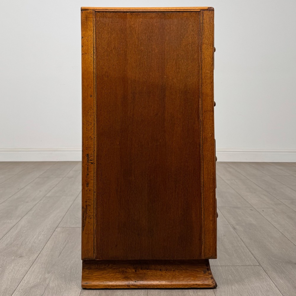 A vintage medium-toned oak chest of drawers featuring four graduated drawers with matching wooden bar handles set on a flared plinth base. View VII