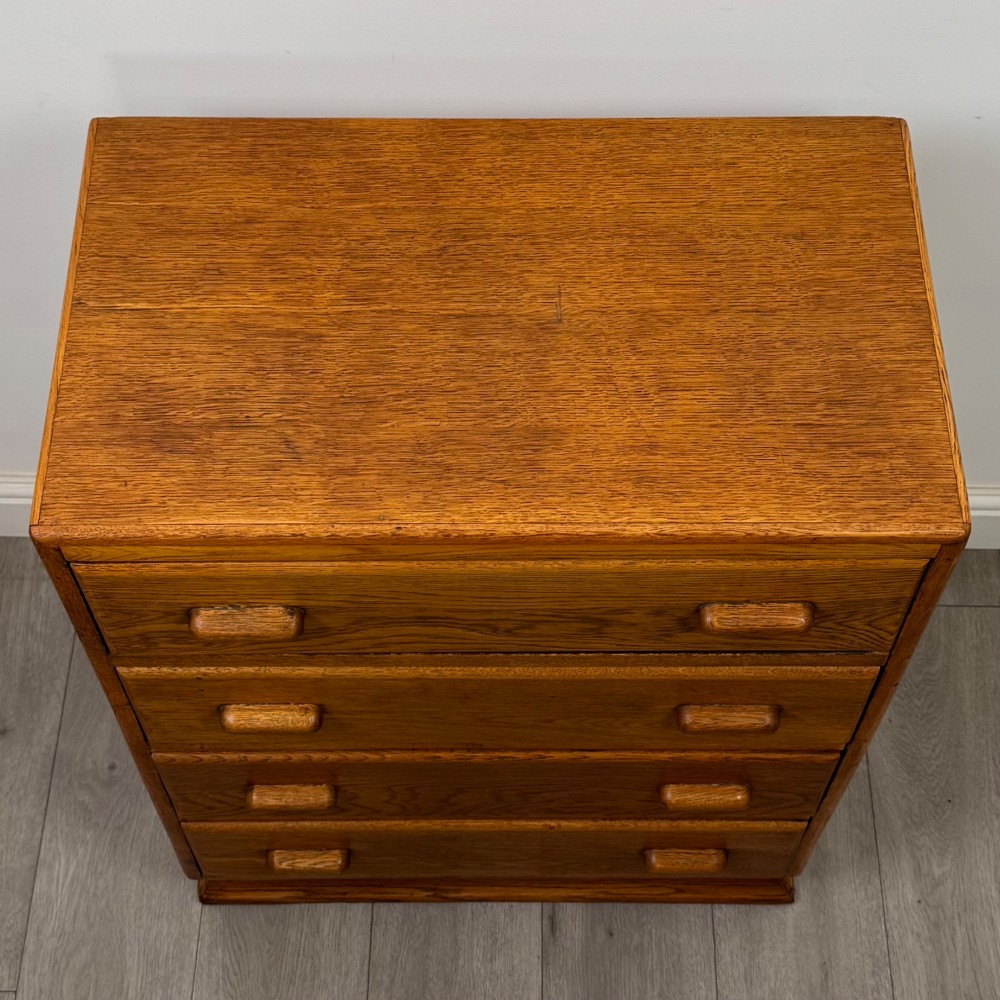A vintage medium-toned oak chest of drawers featuring four graduated drawers with matching wooden bar handles set on a flared plinth base. View IX