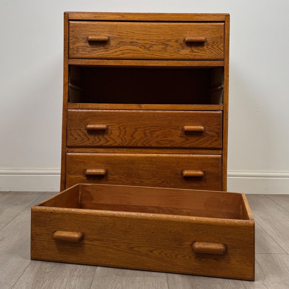 A vintage medium-toned oak chest of drawers featuring four graduated drawers with matching wooden bar handles set on a flared plinth base. View X