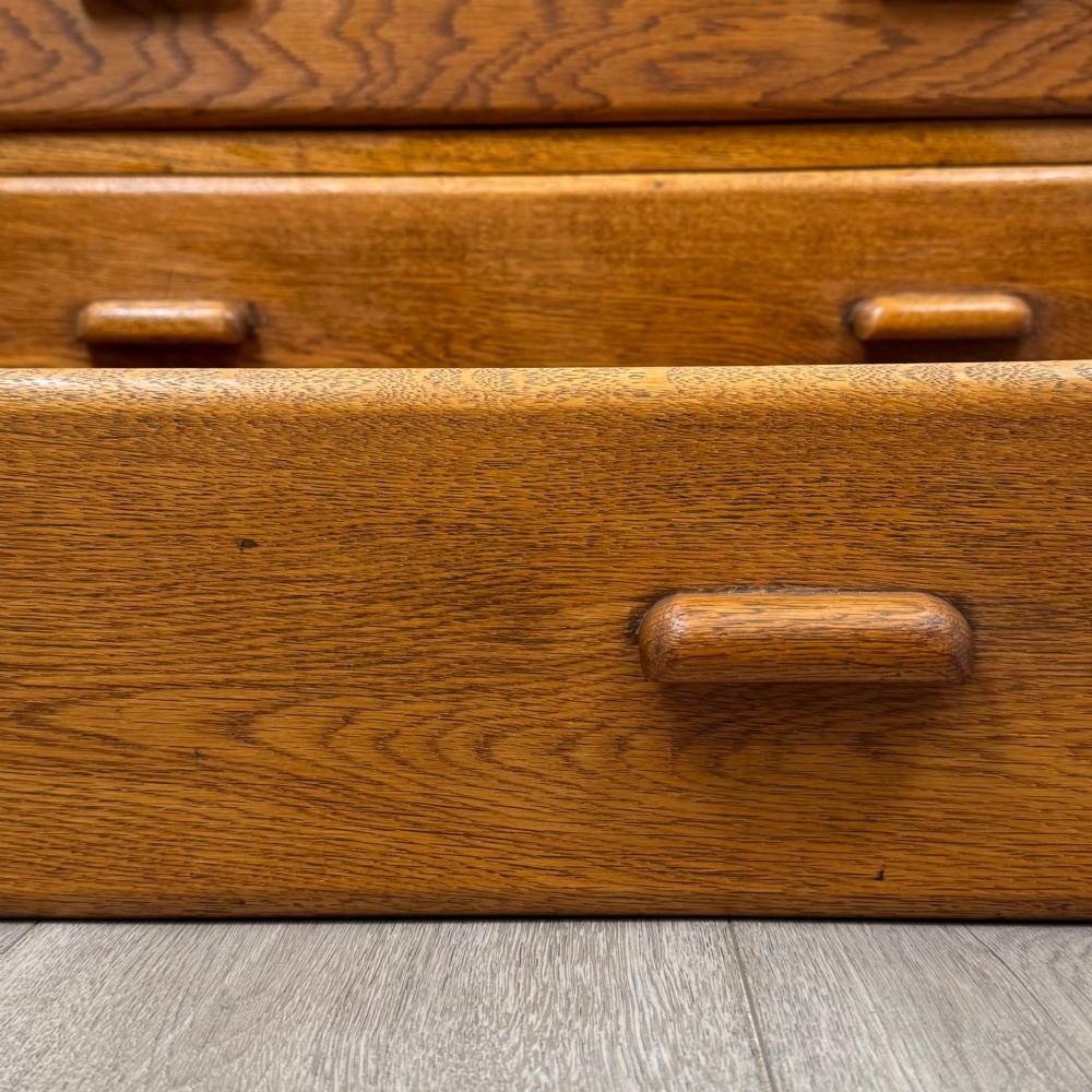 A vintage medium-toned oak chest of drawers featuring four graduated drawers with matching wooden bar handles set on a flared plinth base. View XI
