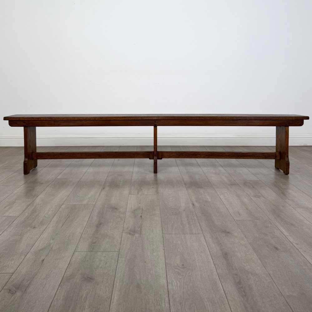 A long 19th-century Georgian oak tavern bench featuring a smooth plank seat supported by three sturdy slab legs and a full-length lower stretcher.