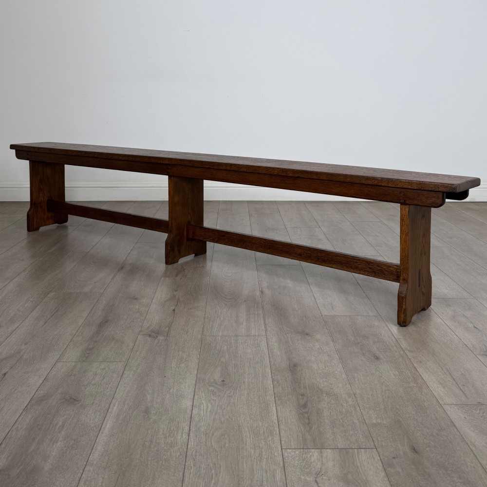A long 19th-century Georgian oak tavern bench featuring a smooth plank seat supported by three sturdy slab legs and a full-length lower stretcher. View II