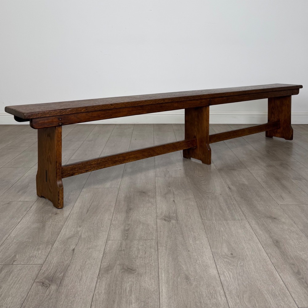 A long 19th-century Georgian oak tavern bench featuring a smooth plank seat supported by three sturdy slab legs and a full-length lower stretcher. View IV