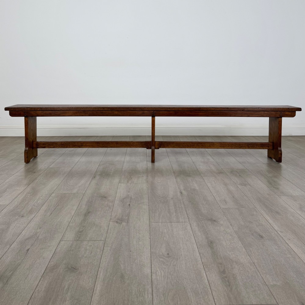 A long 19th-century Georgian oak tavern bench featuring a smooth plank seat supported by three sturdy slab legs and a full-length lower stretcher. View V