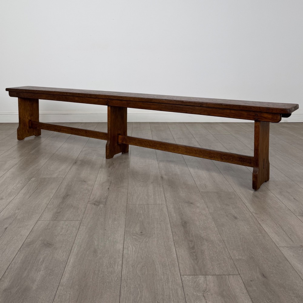 A long 19th-century Georgian oak tavern bench featuring a smooth plank seat supported by three sturdy slab legs and a full-length lower stretcher. View VI