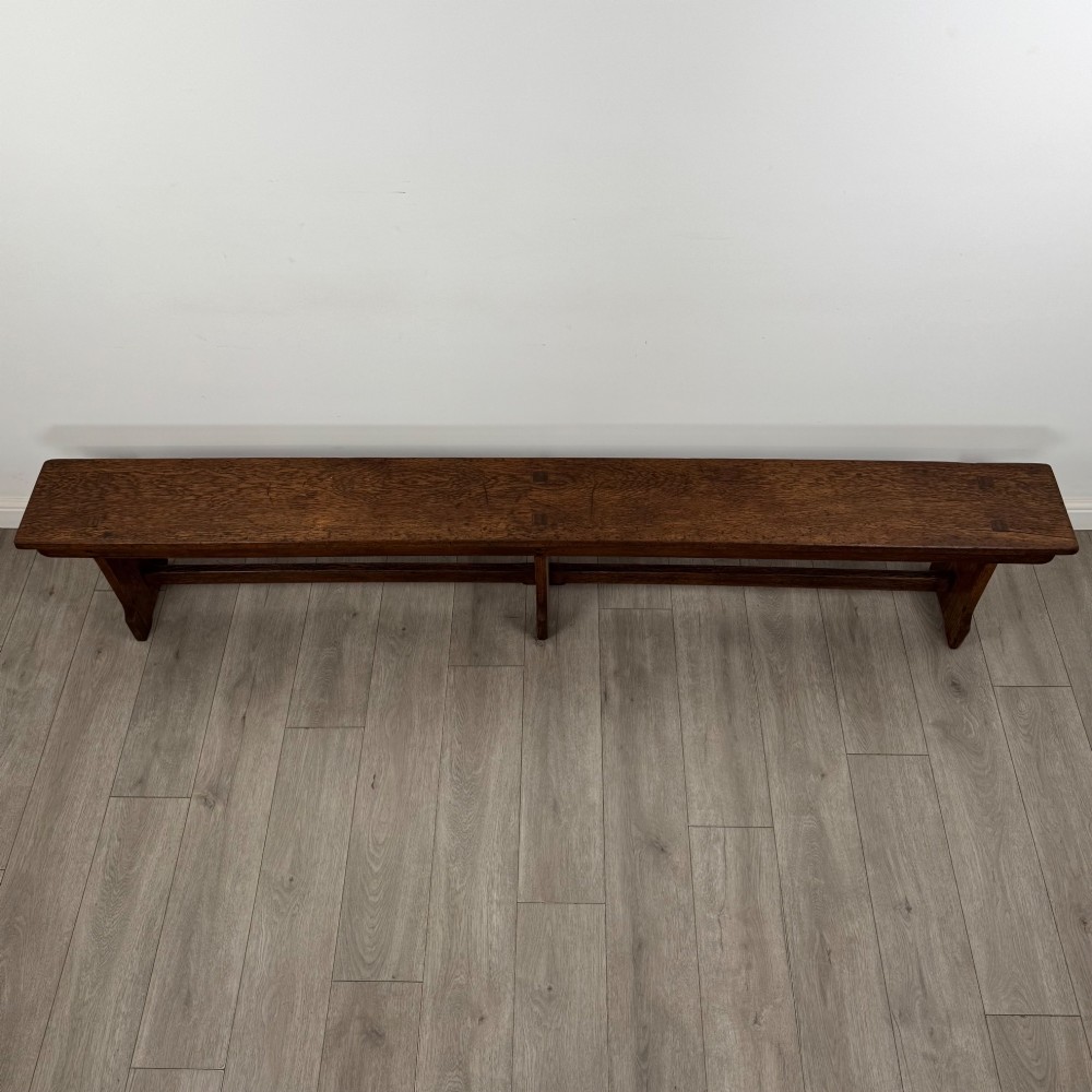 A long 19th-century Georgian oak tavern bench featuring a smooth plank seat supported by three sturdy slab legs and a full-length lower stretcher. View VIII