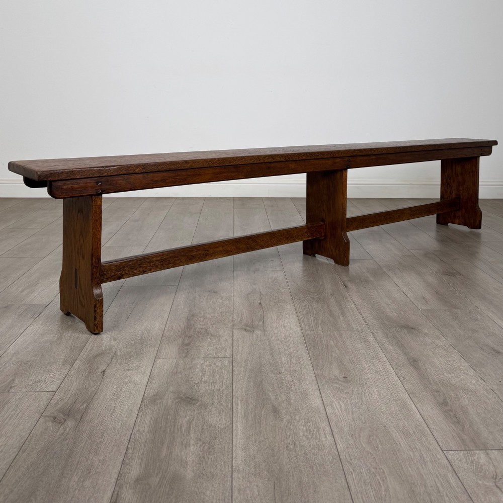 A long 19th-century Georgian oak tavern bench featuring a smooth plank seat supported by three sturdy slab legs and a full-length lower stretcher. View IX