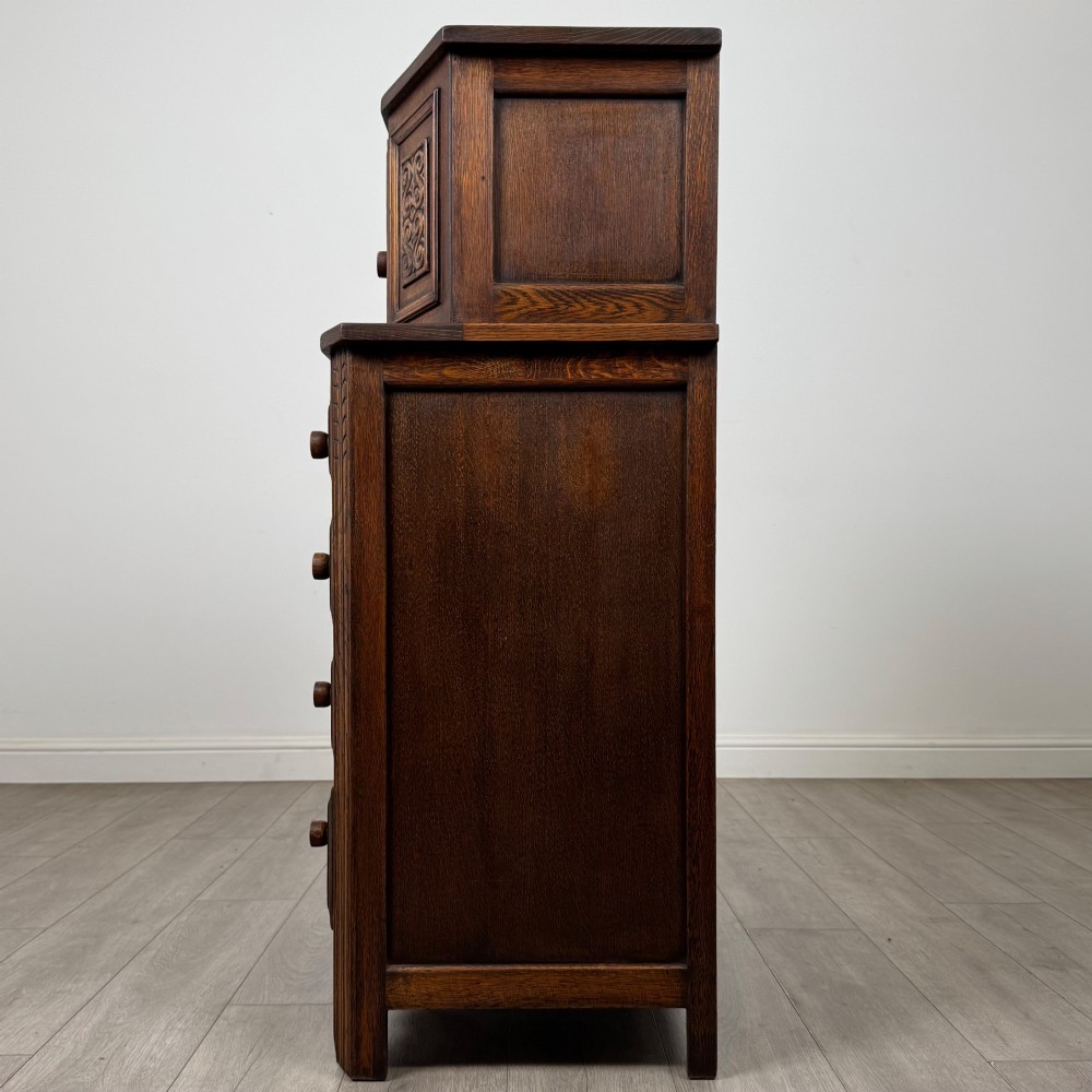An Edwardian dark oak cupboard featuring an upper canted cabinet with carved decorative panels above four graduated drawers with turned wooden knobs. View IV