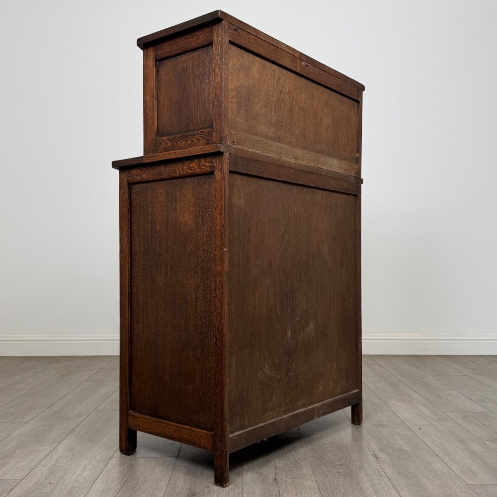 An Edwardian dark oak cupboard featuring an upper canted cabinet with carved decorative panels above four graduated drawers with turned wooden knobs. View V