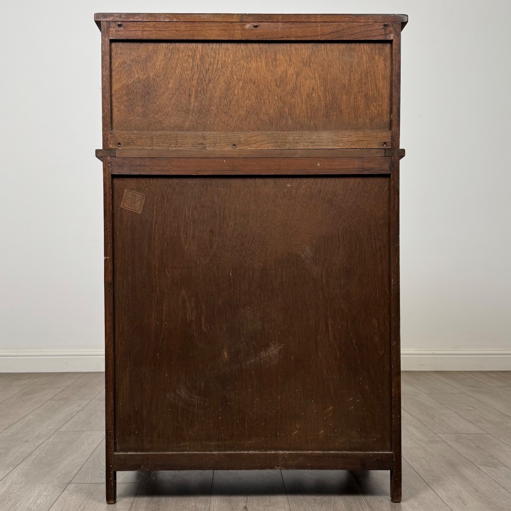 An Edwardian dark oak cupboard featuring an upper canted cabinet with carved decorative panels above four graduated drawers with turned wooden knobs. View VI