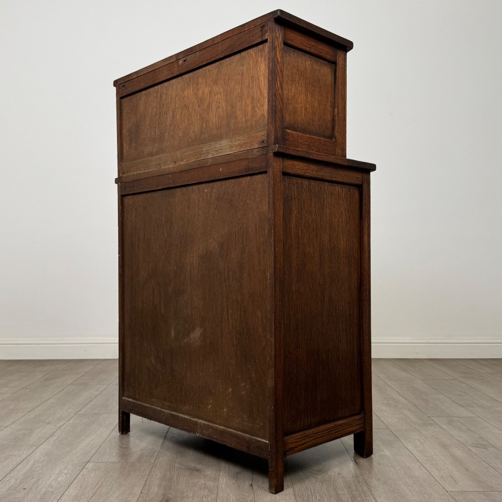 An Edwardian dark oak cupboard featuring an upper canted cabinet with carved decorative panels above four graduated drawers with turned wooden knobs. View VII