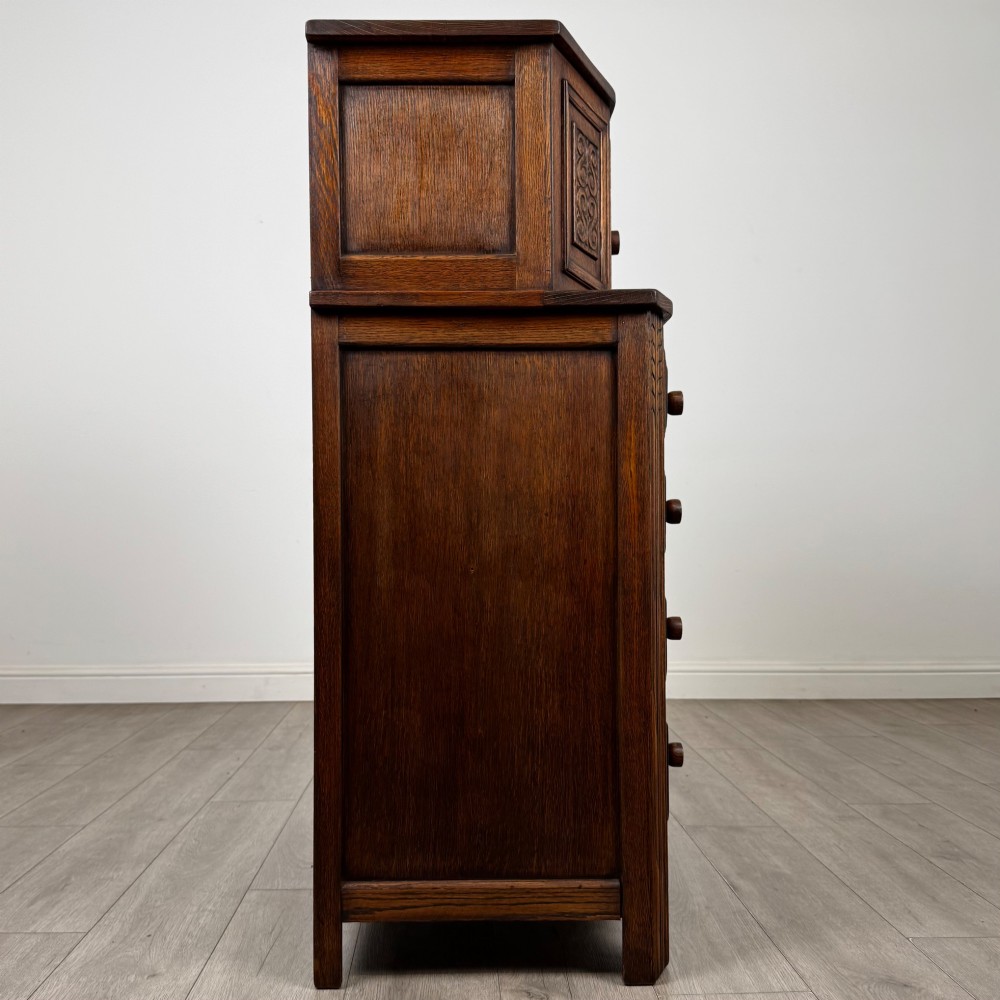 An Edwardian dark oak cupboard featuring an upper canted cabinet with carved decorative panels above four graduated drawers with turned wooden knobs. View VIII