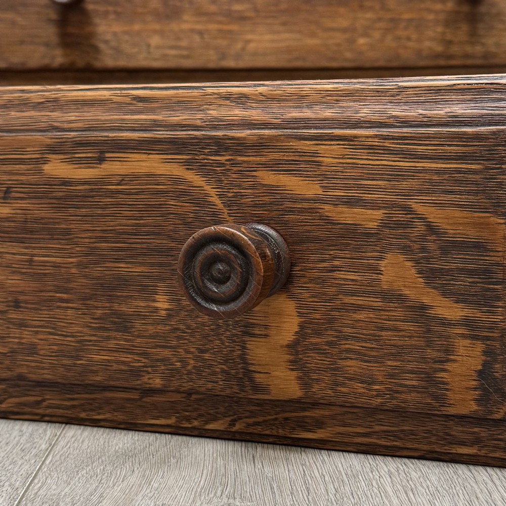 An Edwardian dark oak cupboard featuring an upper canted cabinet with carved decorative panels above four graduated drawers with turned wooden knobs. View XII