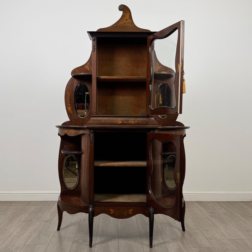 A late 19th-century mahogany display cabinet featuring floral marquetry inlay, glazed central doors, oval side mirrors, and a decorative asymmetric crest pediment. View II