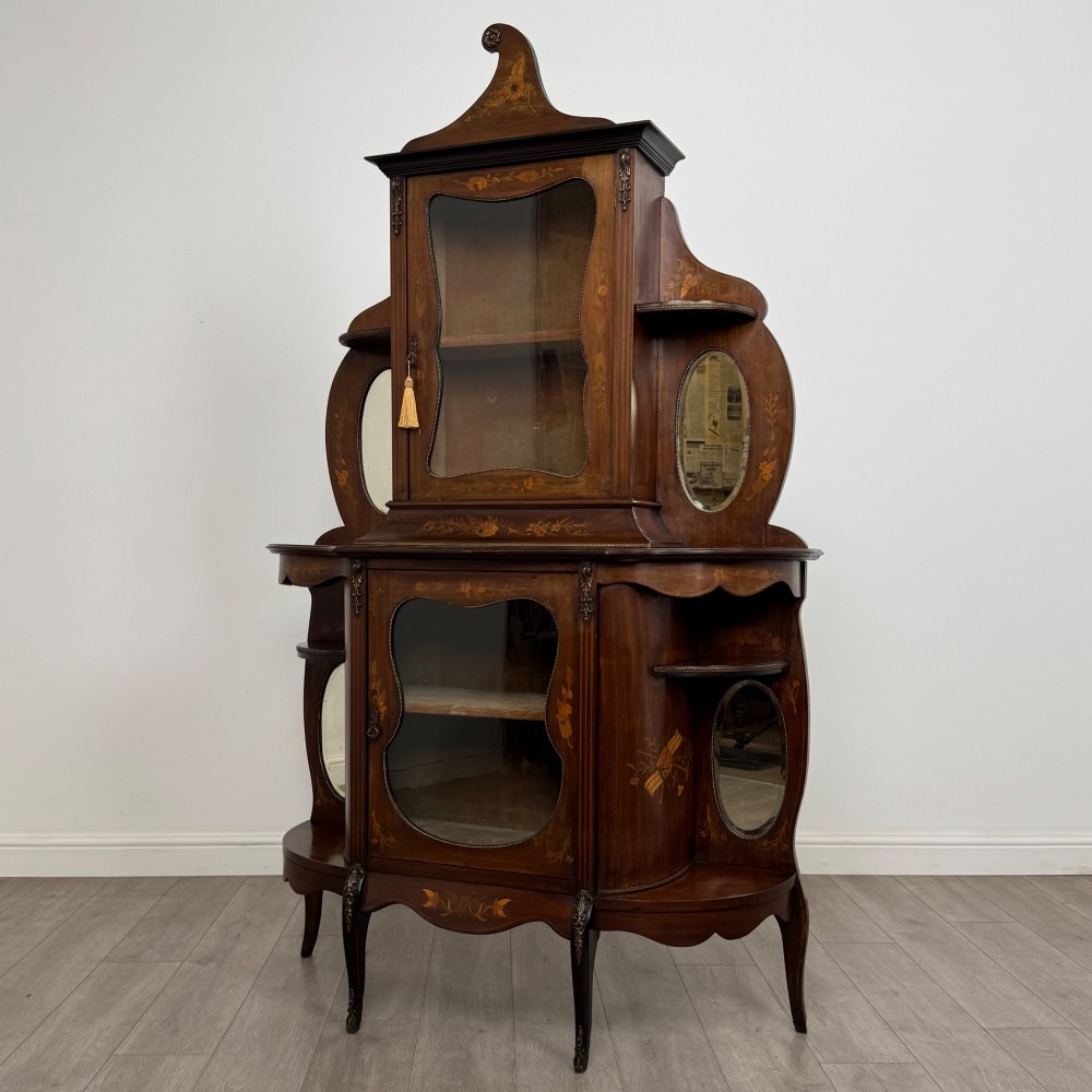 A late 19th-century mahogany display cabinet featuring floral marquetry inlay, glazed central doors, oval side mirrors, and a decorative asymmetric crest pediment. View III
