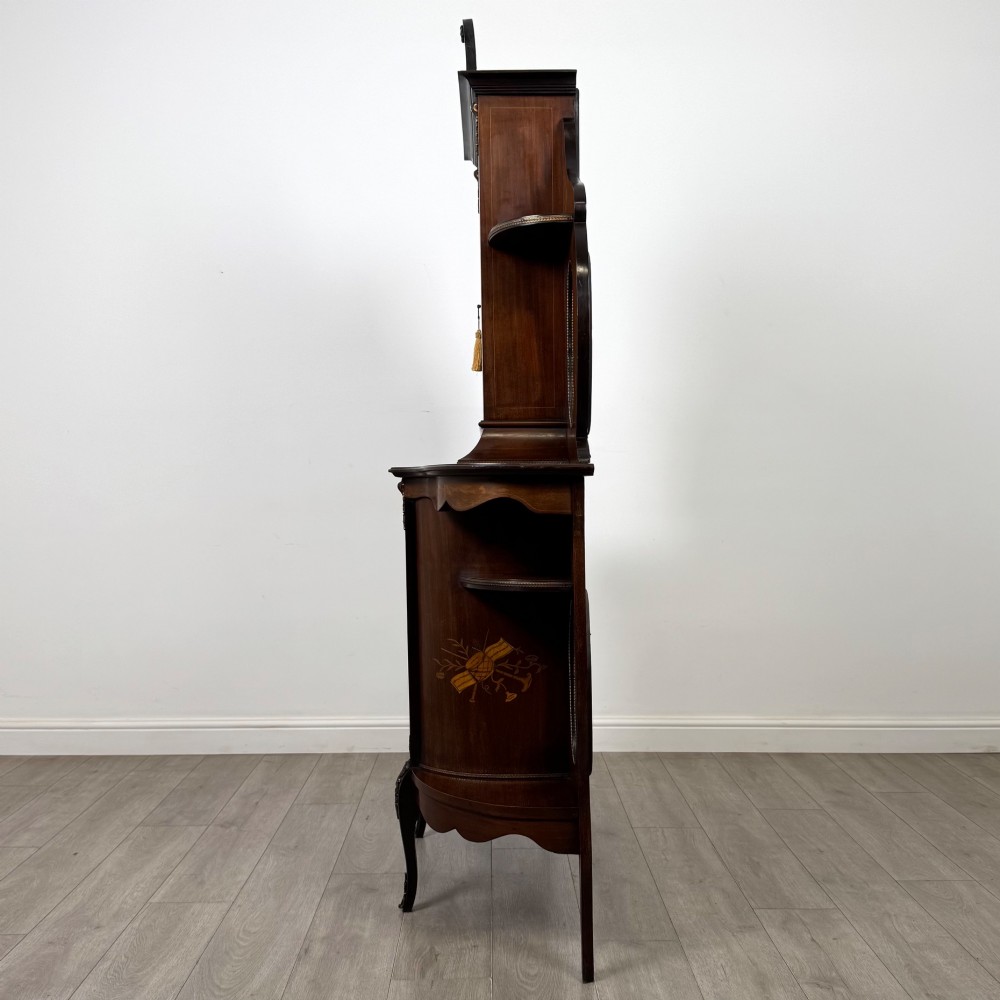 A late 19th-century mahogany display cabinet featuring floral marquetry inlay, glazed central doors, oval side mirrors, and a decorative asymmetric crest pediment. View IV