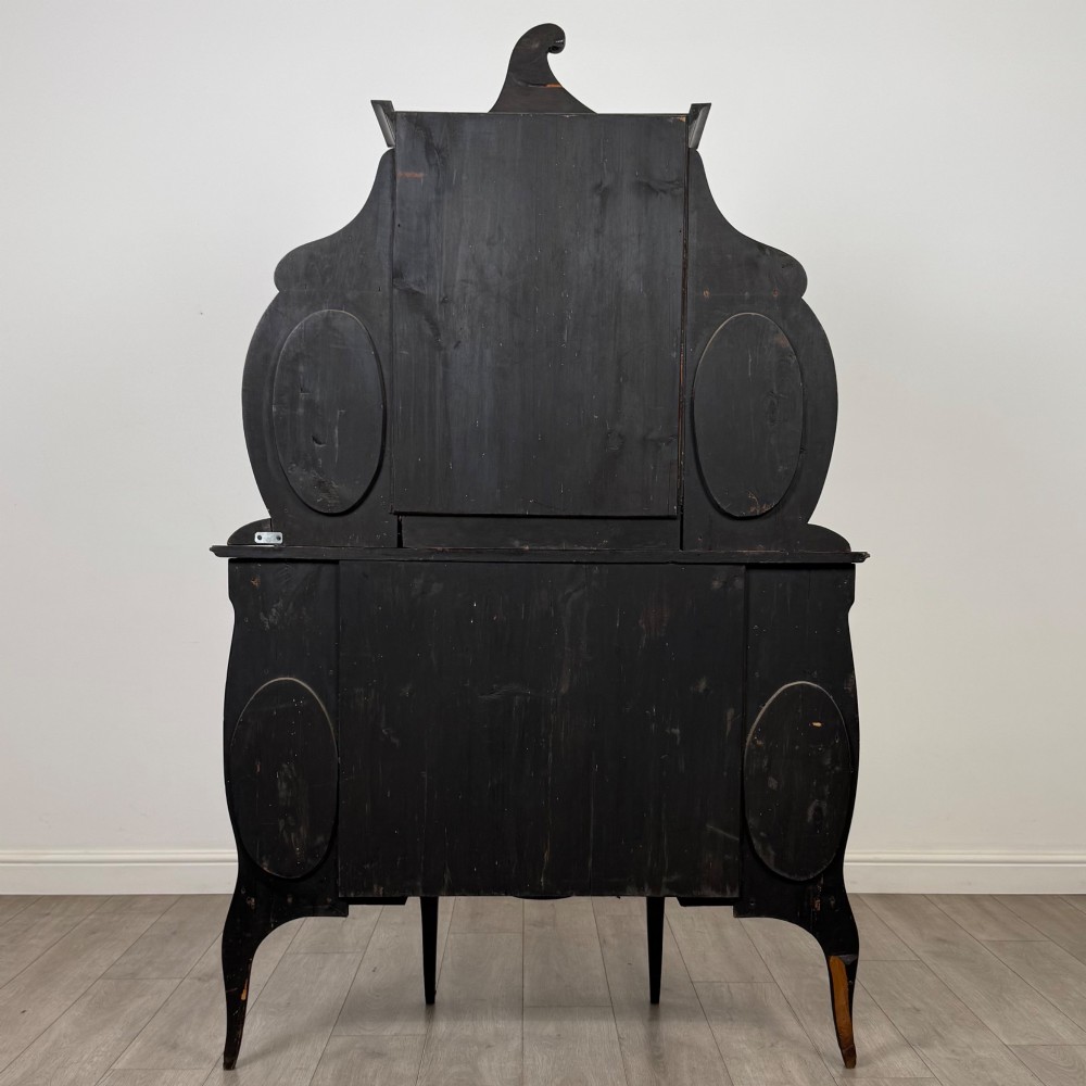 A late 19th-century mahogany display cabinet featuring floral marquetry inlay, glazed central doors, oval side mirrors, and a decorative asymmetric crest pediment. View VI
