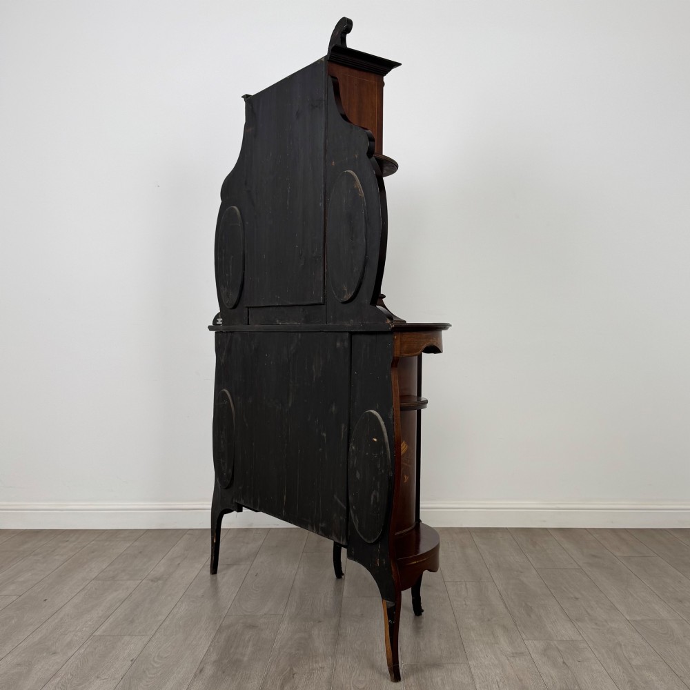 A late 19th-century mahogany display cabinet featuring floral marquetry inlay, glazed central doors, oval side mirrors, and a decorative asymmetric crest pediment. View VII