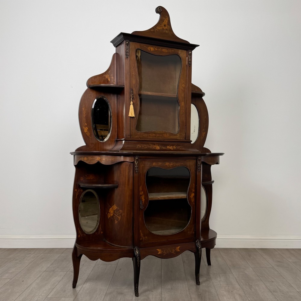 A late 19th-century mahogany display cabinet featuring floral marquetry inlay, glazed central doors, oval side mirrors, and a decorative asymmetric crest pediment. View IX