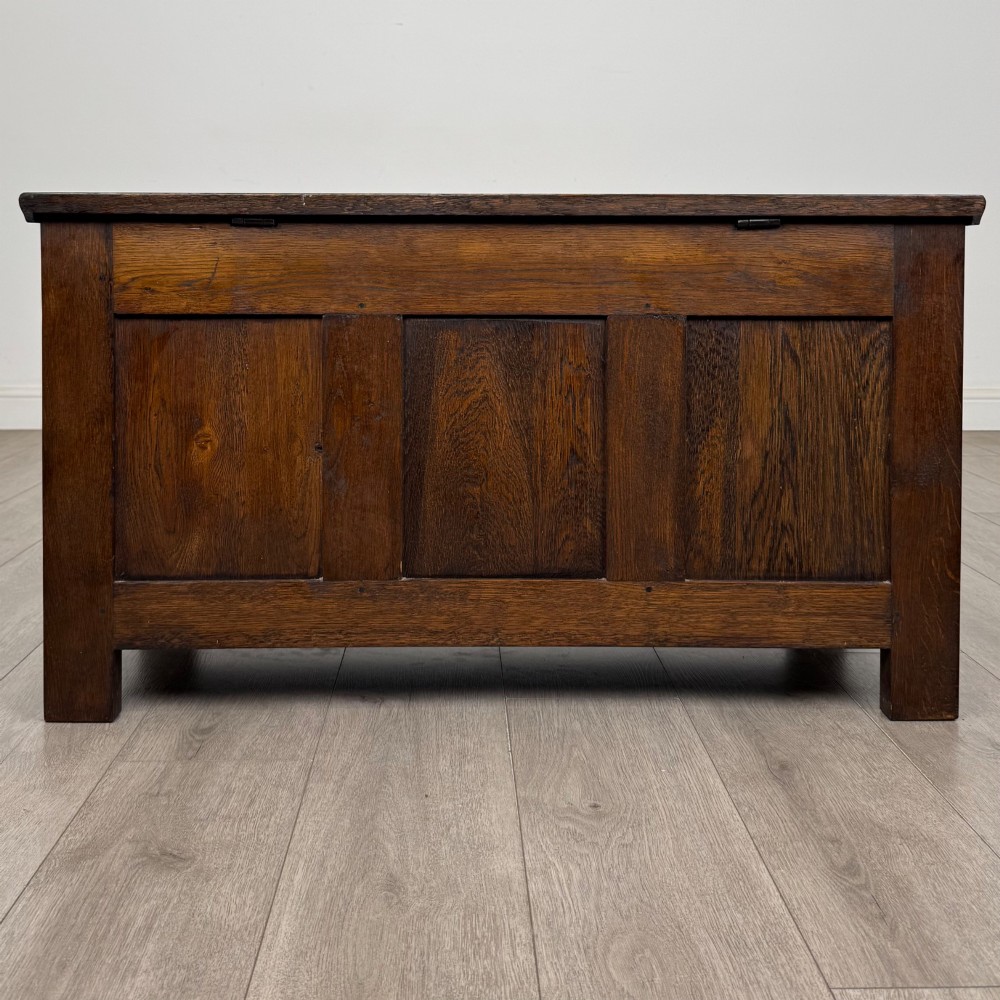 A rectangular dark oak blanket box featuring a hinged top lid, panelled front sections, and carved arch motifs along the upper frieze. View V